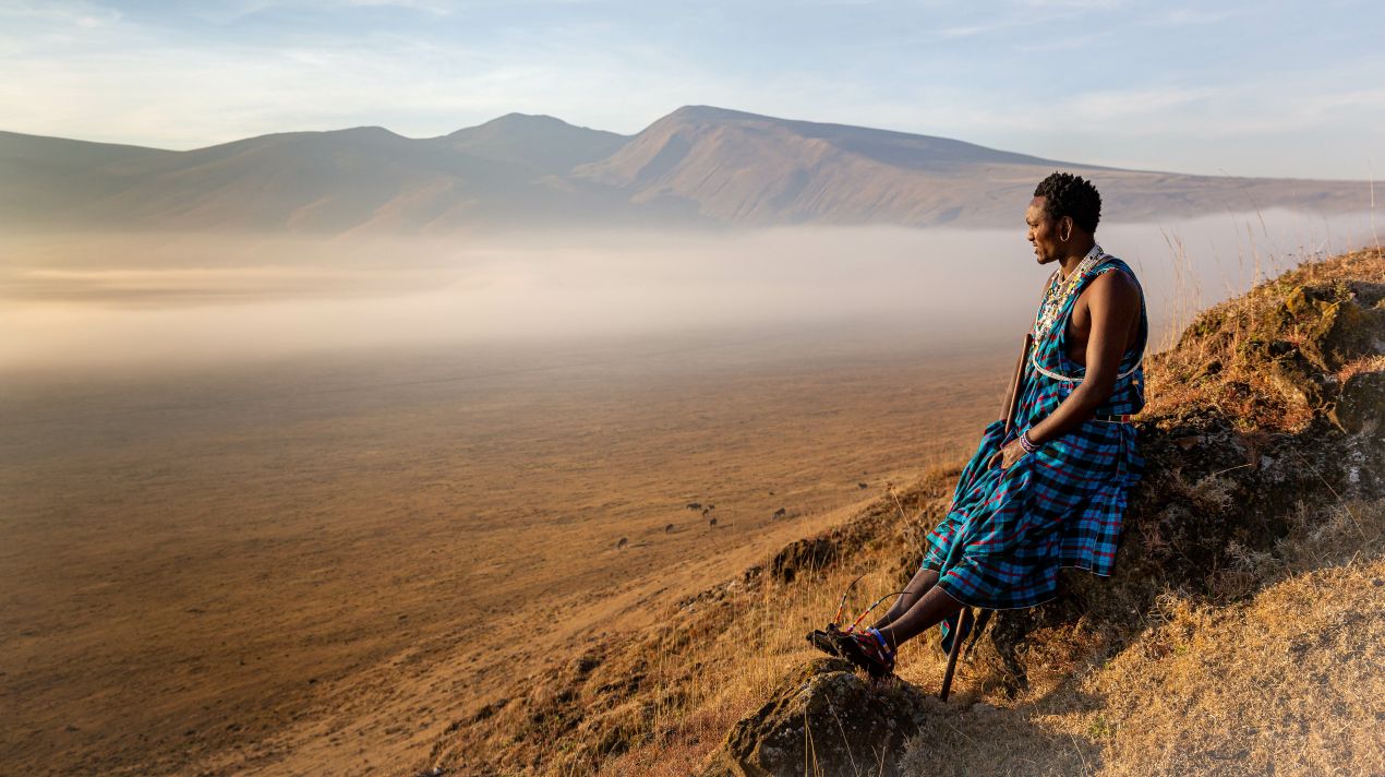 Eine Maasai-Frau sitzt auf einem Hügel und blickt über die weite Landschaft des Ngorongoro-Kraters – ein Highlight jeder Tansania Safari.