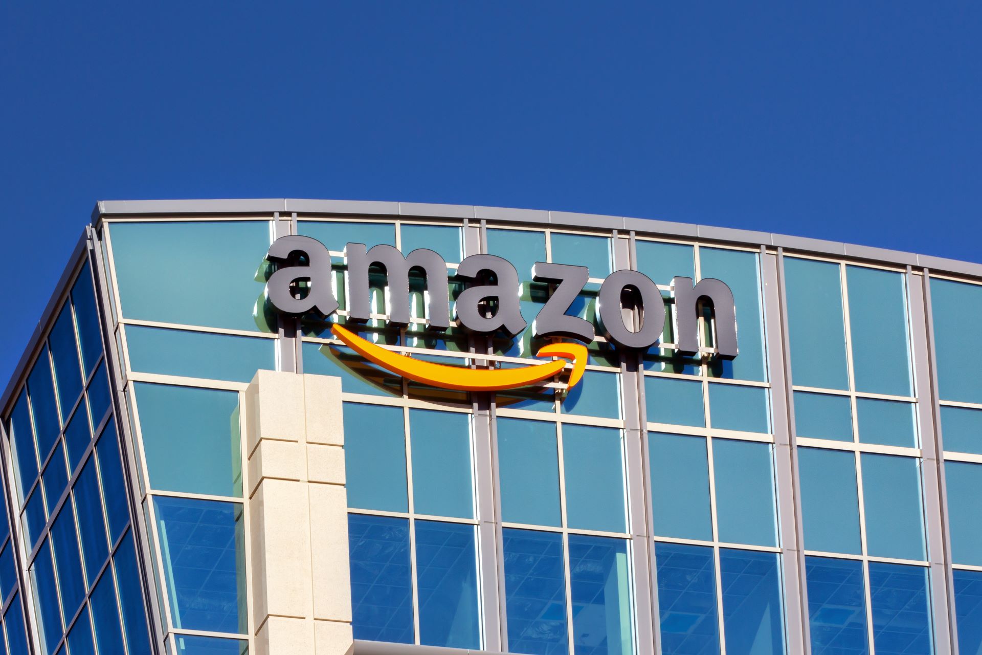 Amazon-Logo auf einem modernen Bürogebäude mit Glasfassade vor blauem Himmel