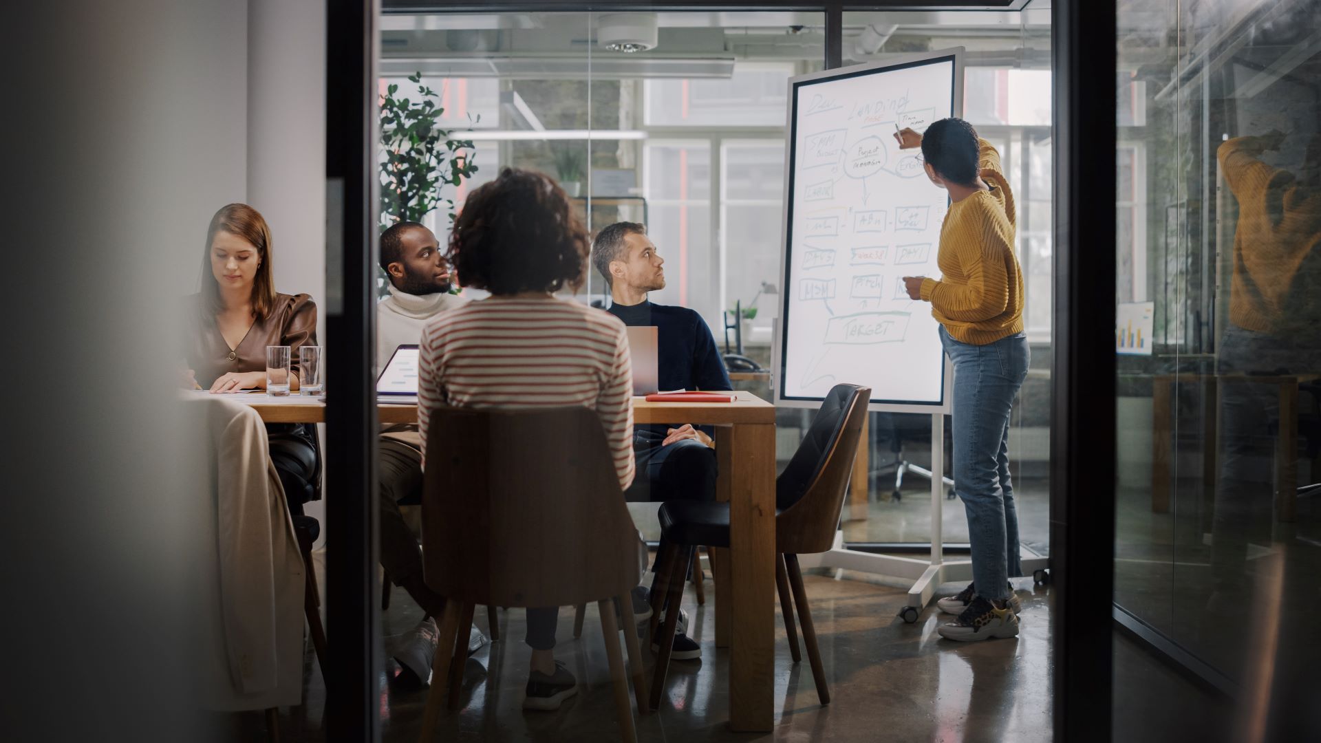 Team in einem Besprechungsraum: Eine Frau präsentiert Ideen an einem Whiteboard vor aufmerksamen Kollegen