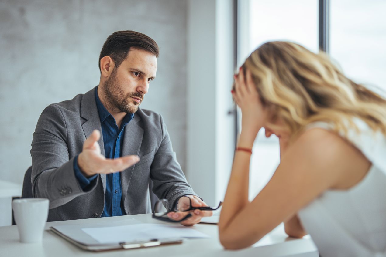 Ein Mann fuehrt ein ernstes Gespraech mit einer gestressten Kollegin, Beispiel fuer Konfliktloesung am Arbeitsplatz durch ehrlichen Dialog und Empathie